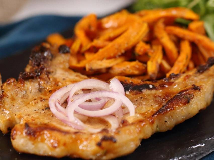 Χοιρινή μπριζόλα με γλυκοπατάτες τηγανητές και φέτες κόκκινου κρεμμυδιού.